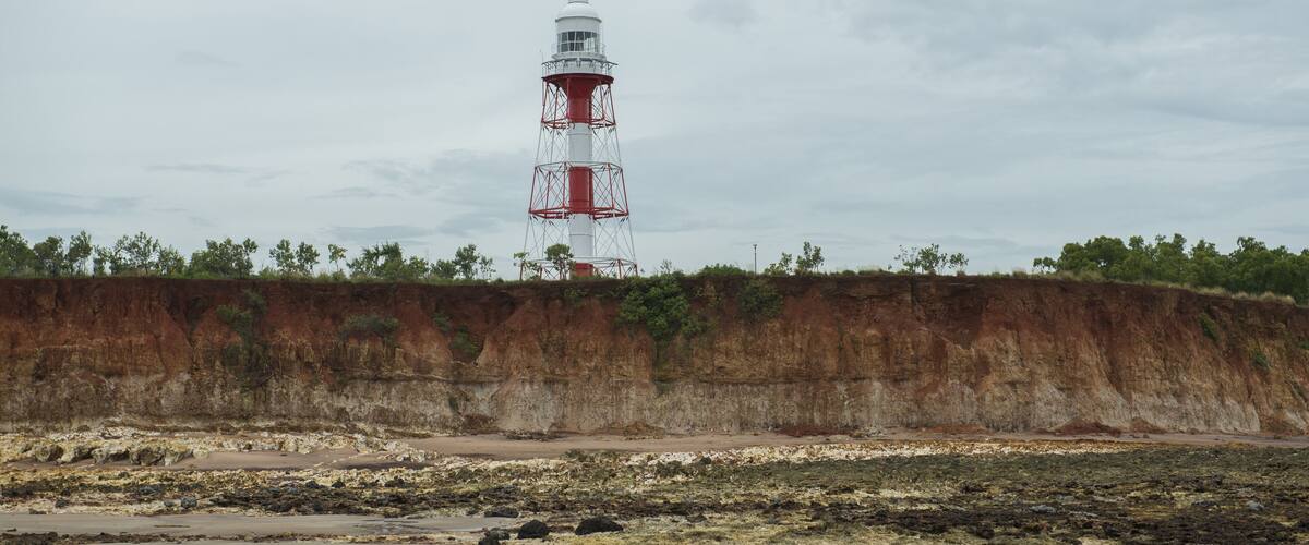 A lighthouse on a rocky shore with a cliff in the background.