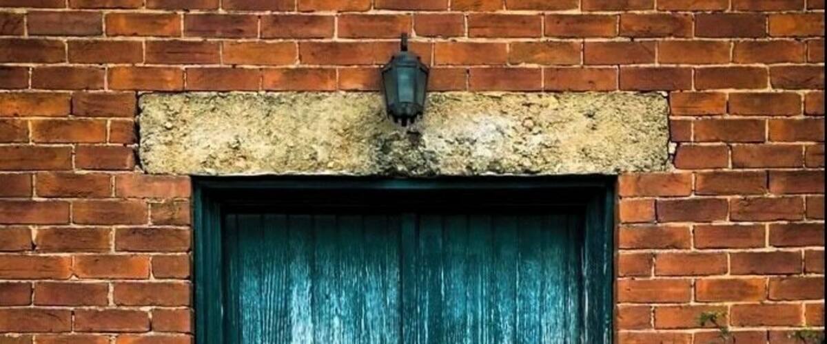 A weathered green door with a brick wall and a small step leading up to it.