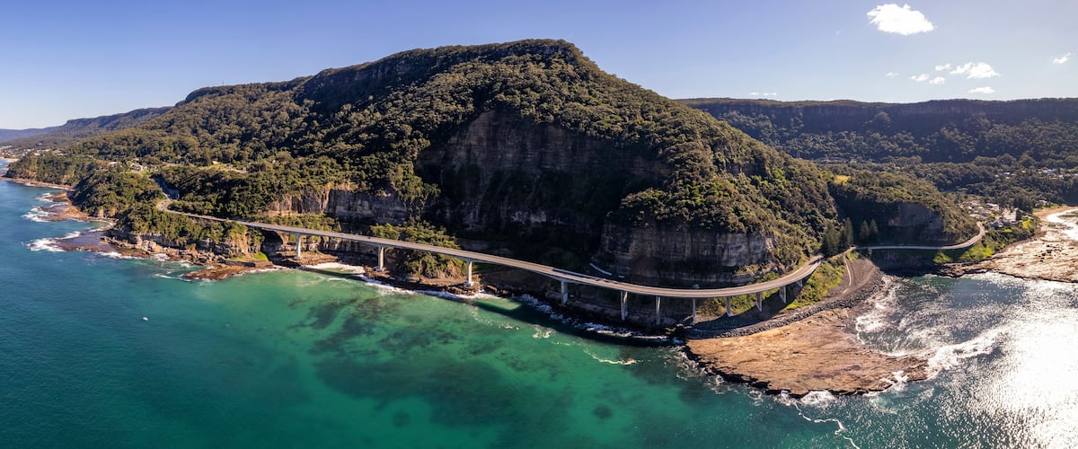 A coastal landscape with a prominent cliff, a bridge, and clear turquoise waters.