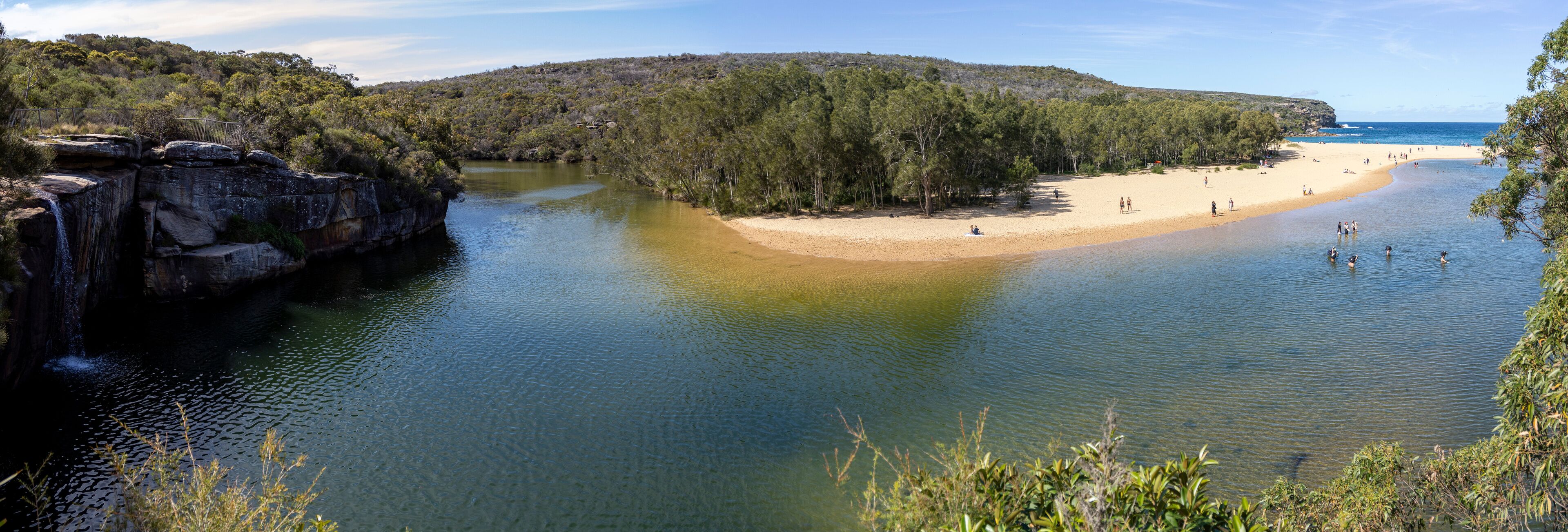 A river leading to a sandy beach surrounded by dense forest and rocky cliffs.