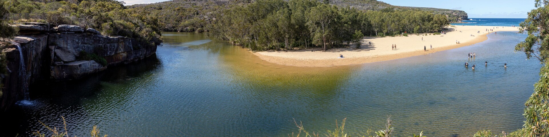A river leading to a sandy beach surrounded by dense forest and rocky cliffs.
