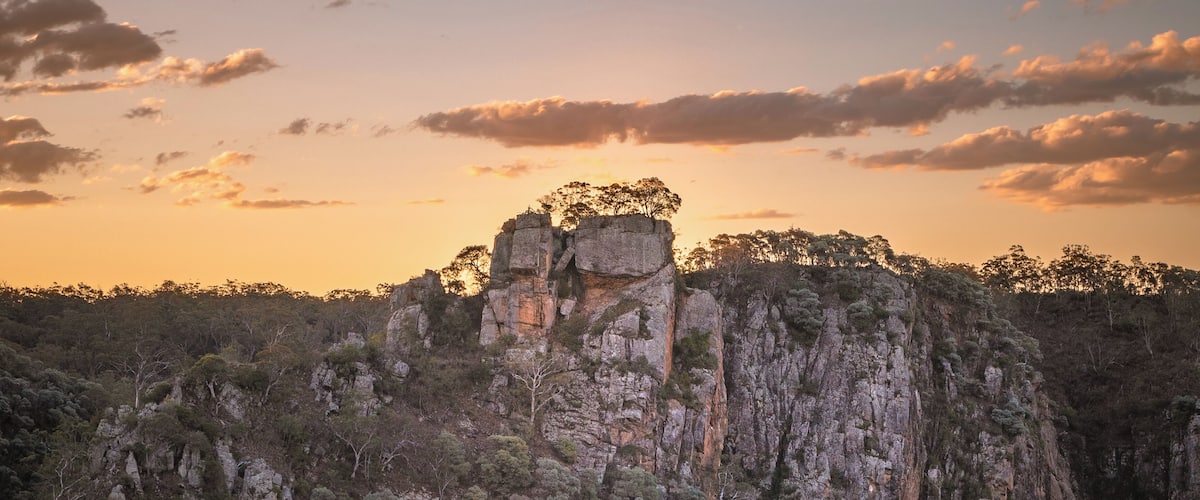 A rugged cliff with a large rock formation and a small structure on top.