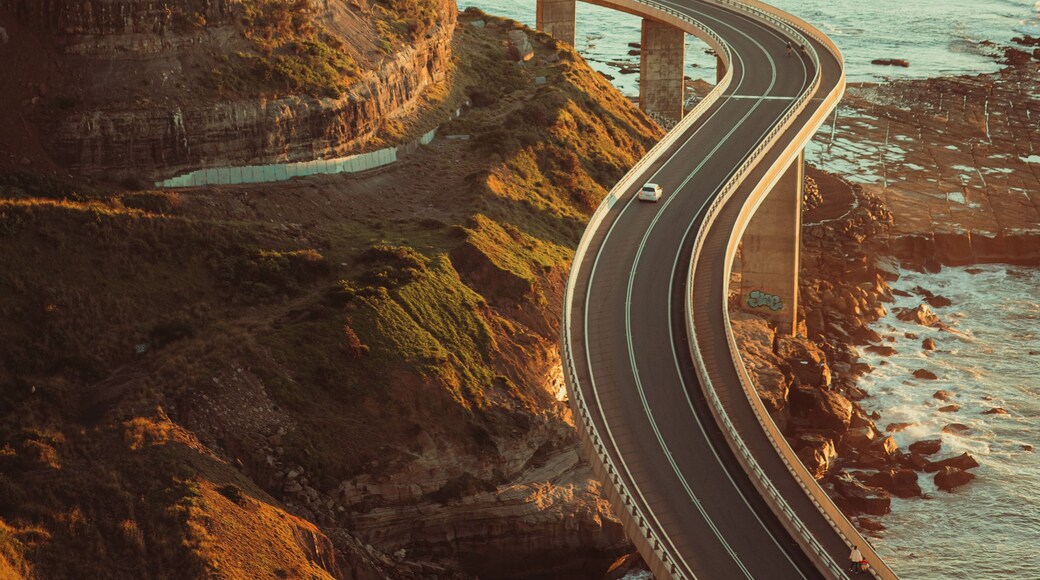 A coastal highway curving along a cliffside with a bridge crossing over the water.