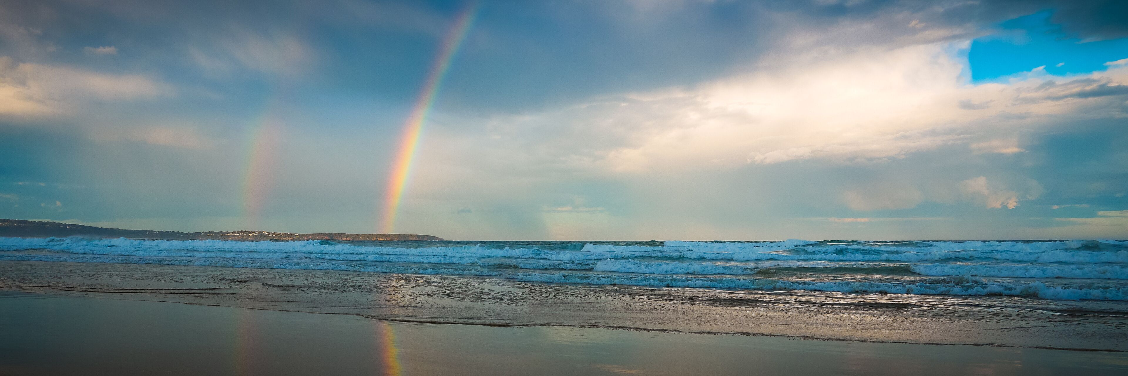 A beach with waves and a rainbow.