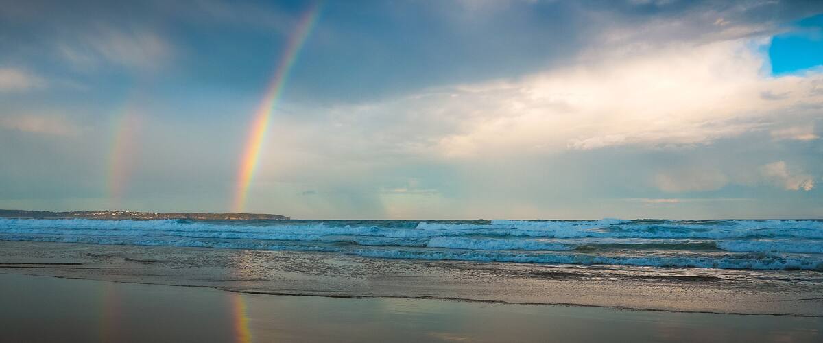 A beach with waves and a rainbow.