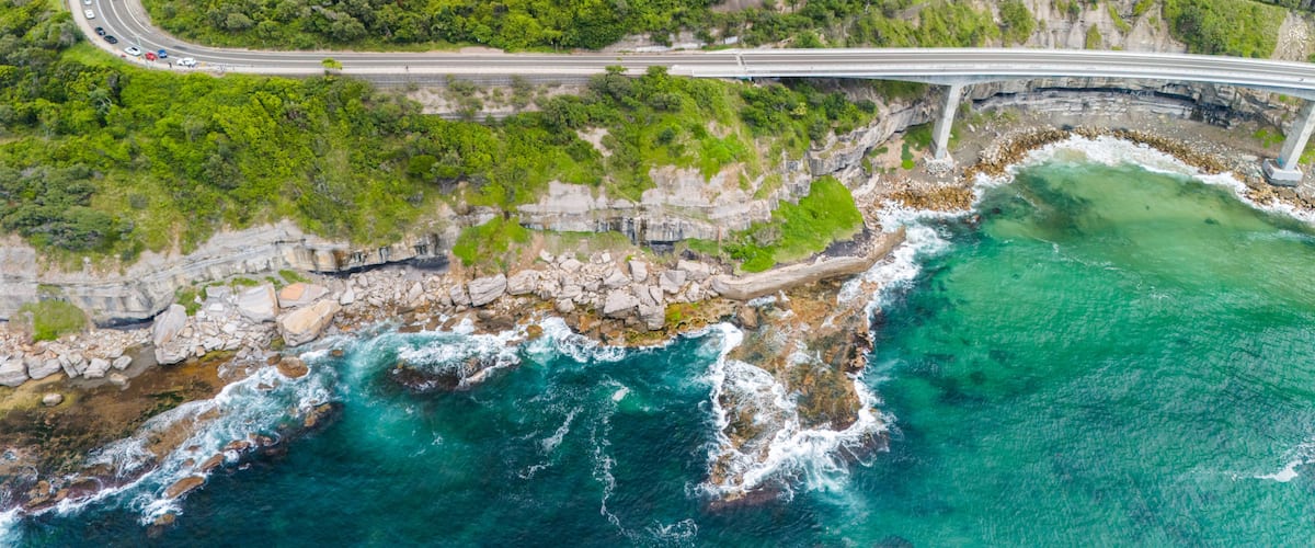 A coastal highway with a bridge over the ocean, surrounded by cliffs and dense greenery.