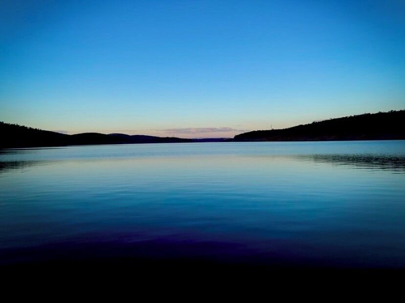 A calm lake with a clear sky and distant hills.