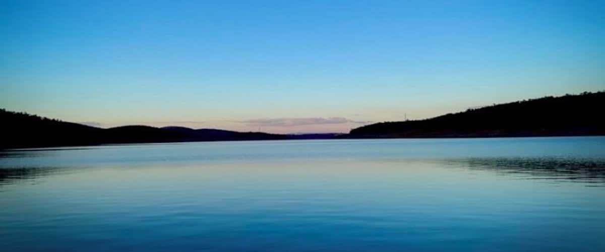 A calm lake with a clear sky and distant hills.