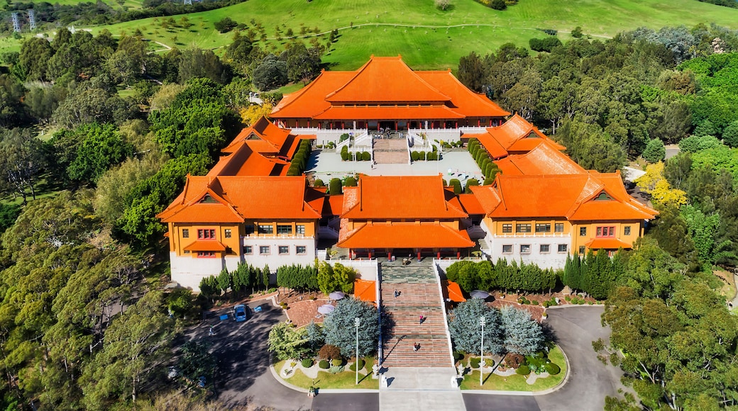 A traditional building with a symmetrical roof and multiple wings, surrounded by lush greenery and hills.