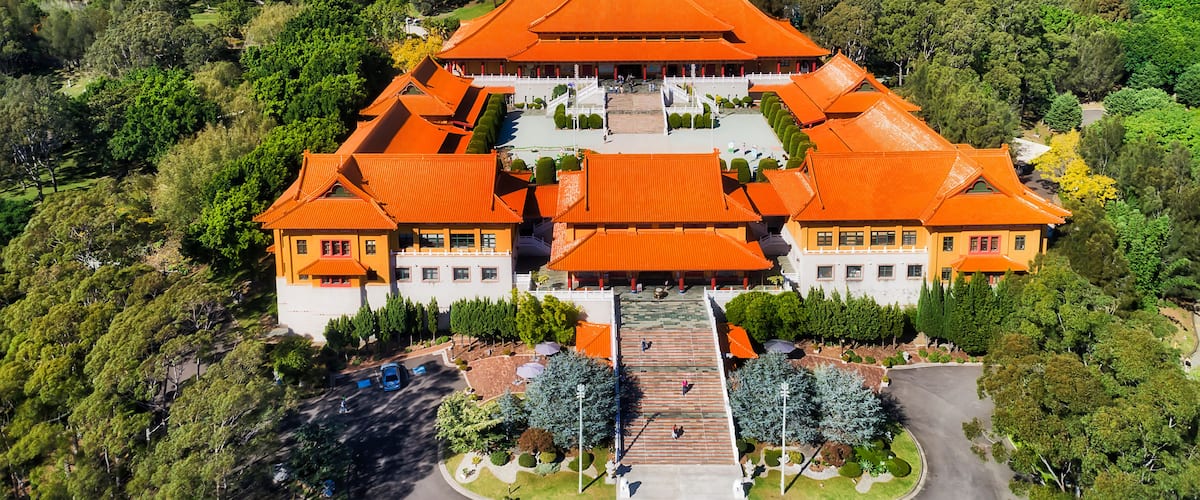 Un edificio tradicional con techo simétrico y varias alas, rodeado de exuberante vegetación y colinas.