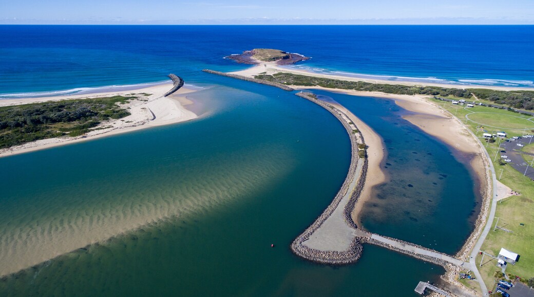 An aerial view of a coastal area with a curved waterway, a small island, and a beach.