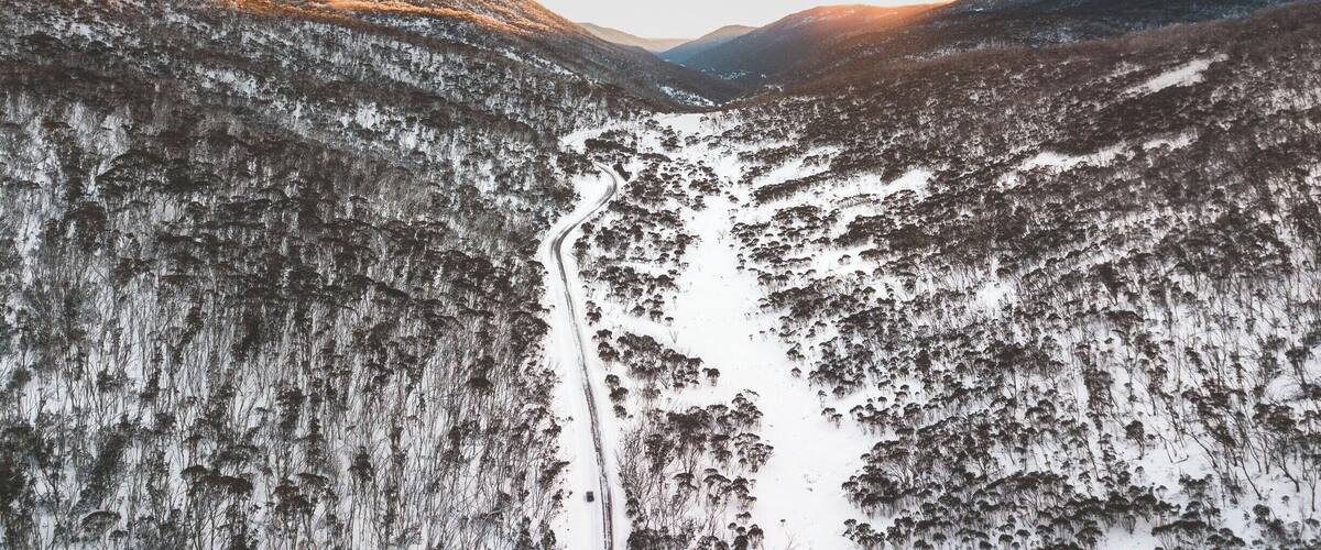 A snow-covered valley with a winding road between forested hills.