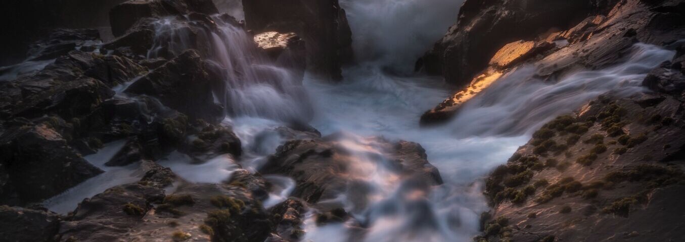 Litoral rochoso com uma cascata ao pôr do sol.