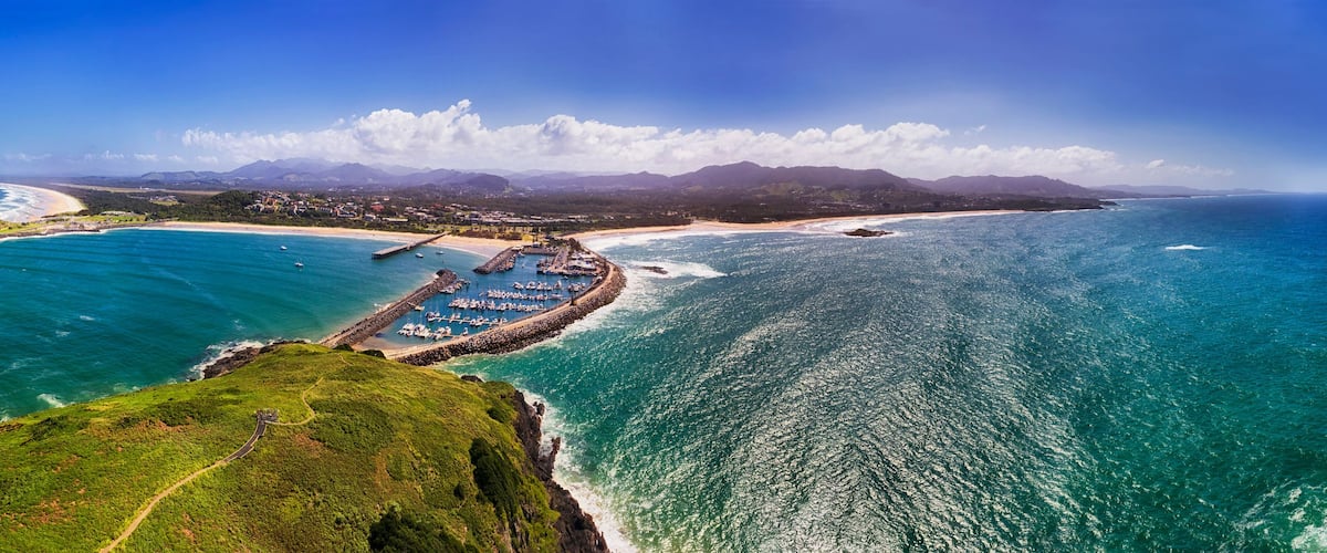 A coastal landscape with a beach, a marina, and a mountainous backdrop.