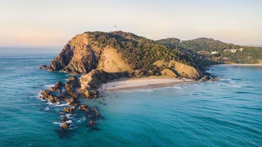 Aerial shot at sunrise over the ocean and white sand beach with swimmers and surfers enjoying summer