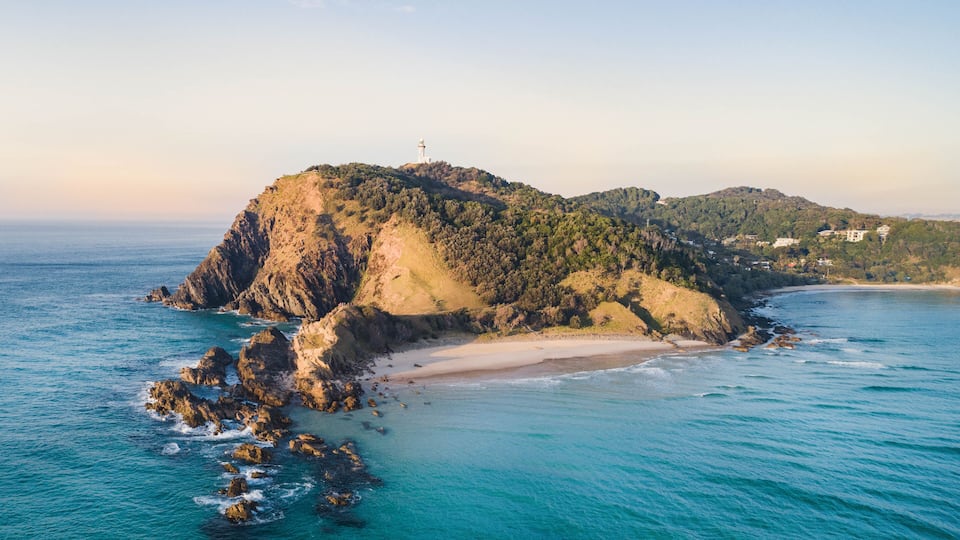 A coastal landscape with a prominent rocky island, a lighthouse, and a beach.