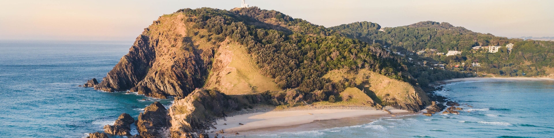 Aerial shot at sunrise over the ocean and white sand beach with swimmers and surfers enjoying summer