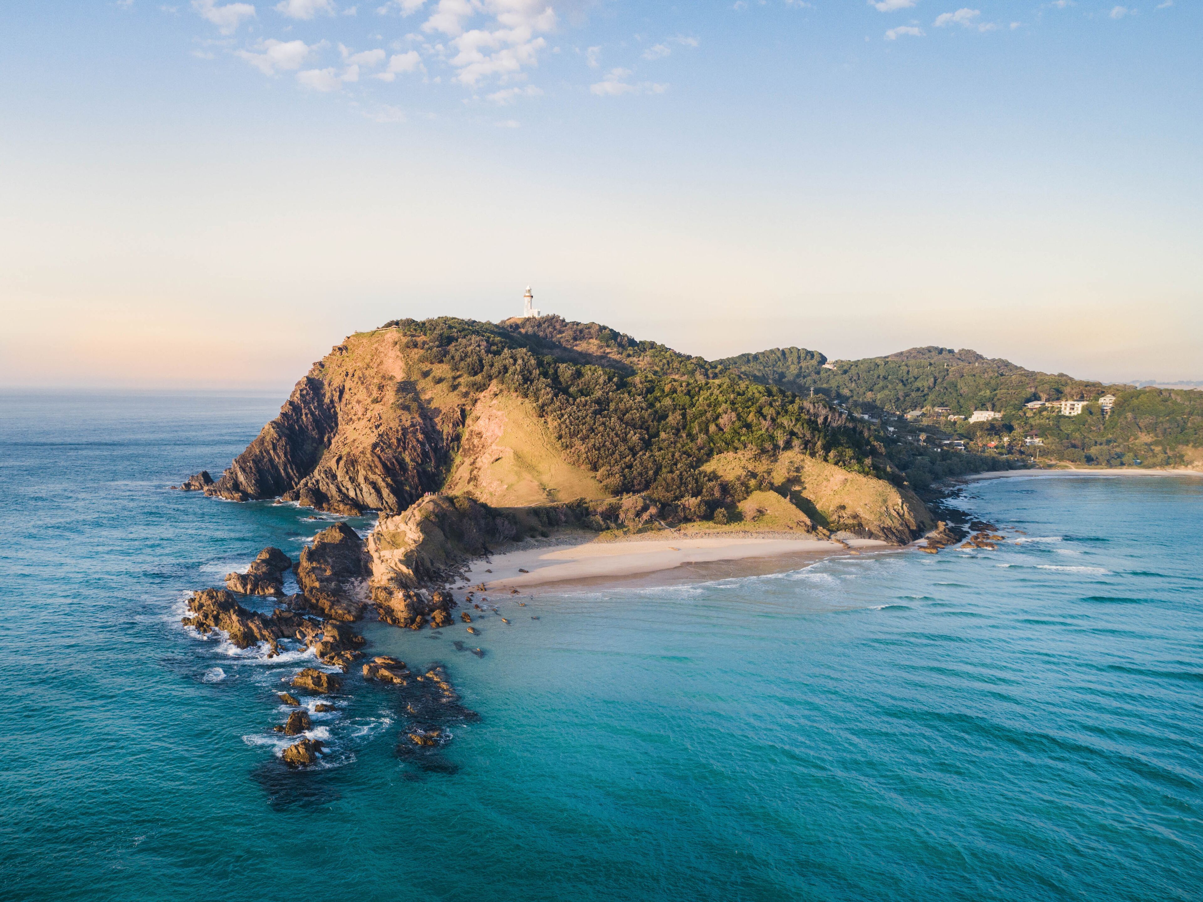 A coastal landscape with a prominent rocky island, a lighthouse, and a beach.