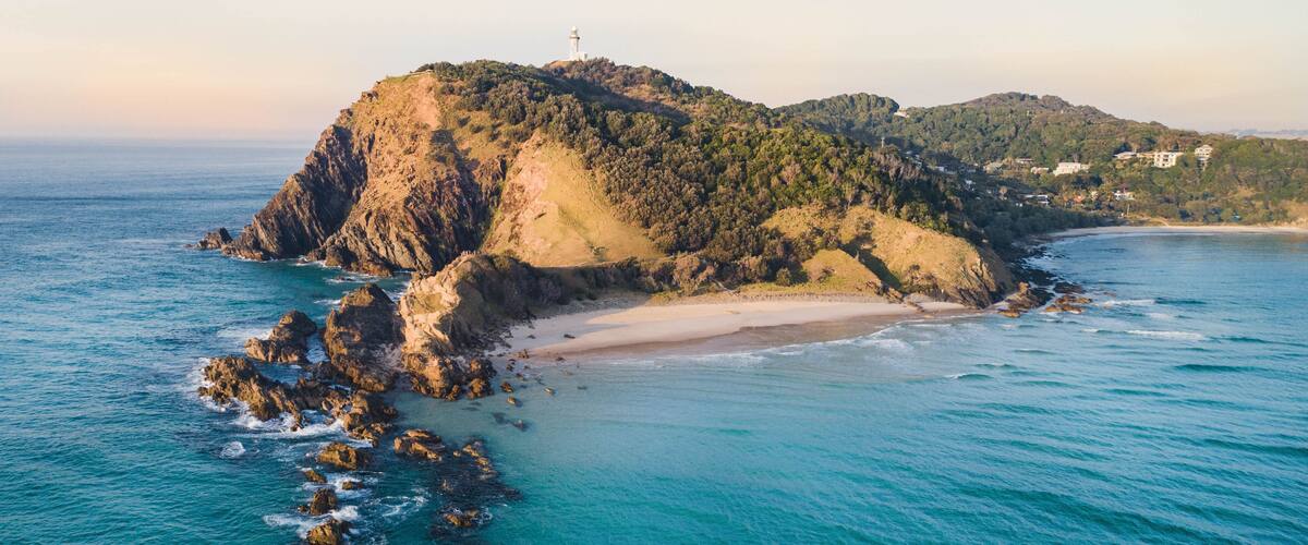 A coastal landscape with a prominent rocky island, a lighthouse, and a beach.