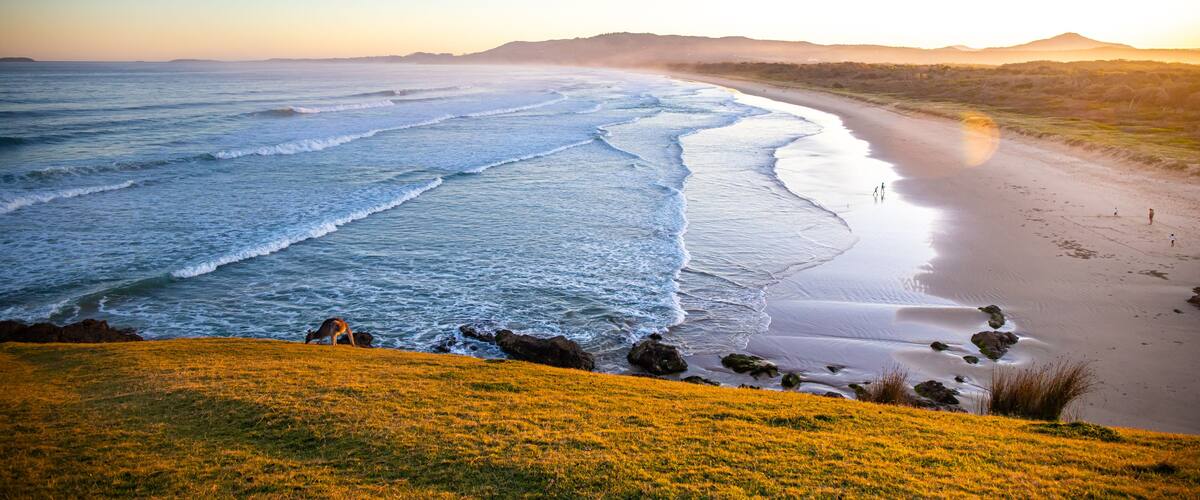 Un paysage côtier avec des vagues, une plage de sable et une colline herbeuse.