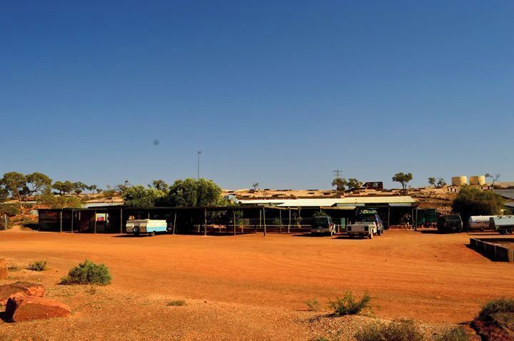 A rural landscape with a dirt road, a building with a corrugated metal roof, and sparse vegetation.