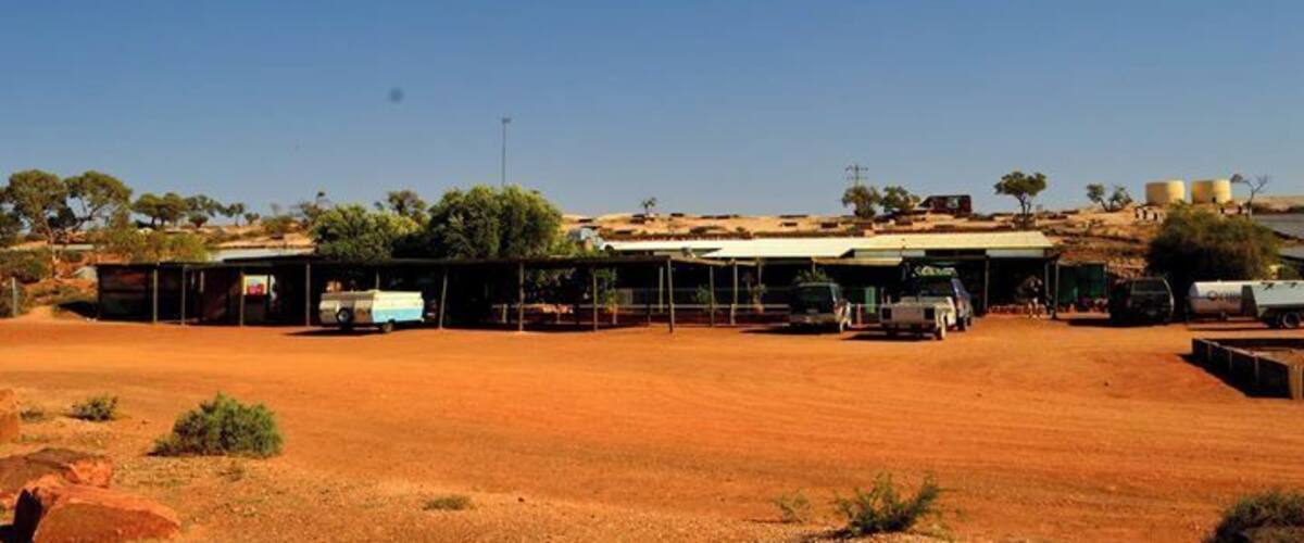 A rural landscape with a dirt road, a building with a corrugated metal roof, and sparse vegetation.