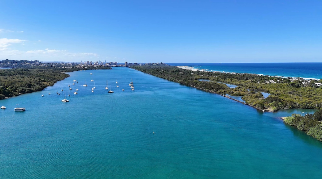 A coastal city with a clear blue sea, numerous boats, and a dense urban skyline in the background.