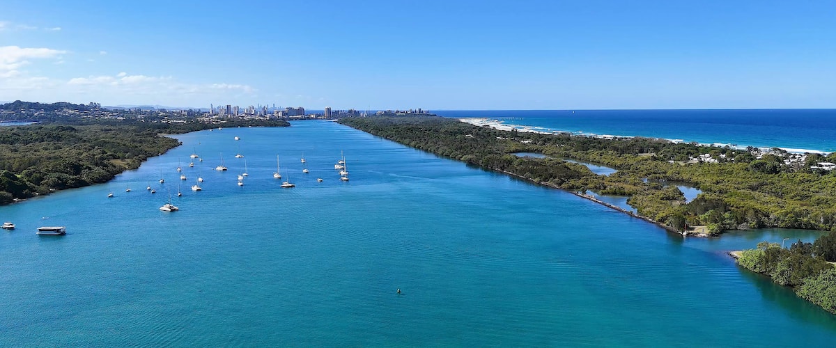 A coastal city with a clear blue sea, numerous boats, and a dense urban skyline in the background.