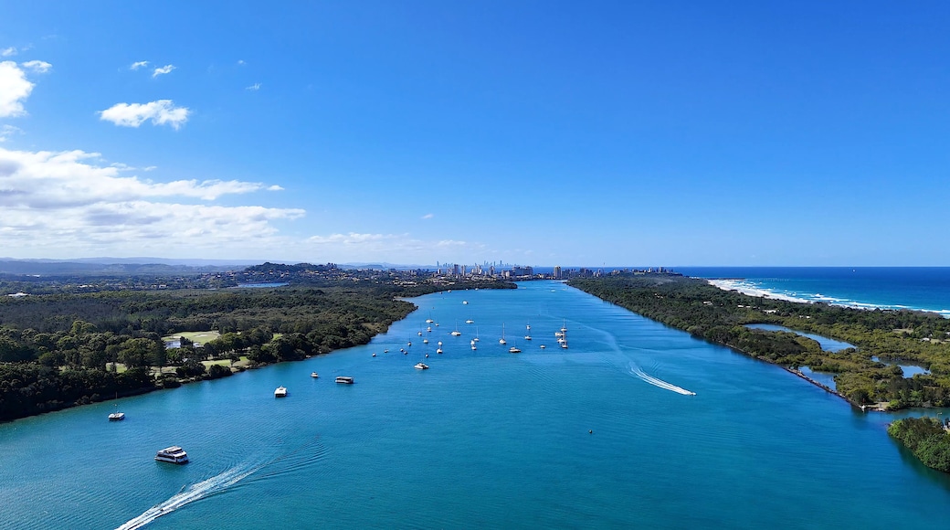 A coastal city with a dense urban skyline, a river with numerous boats, and a clear blue sky.