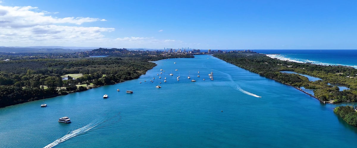 A coastal city with a dense urban skyline, a river with numerous boats, and a clear blue sky.