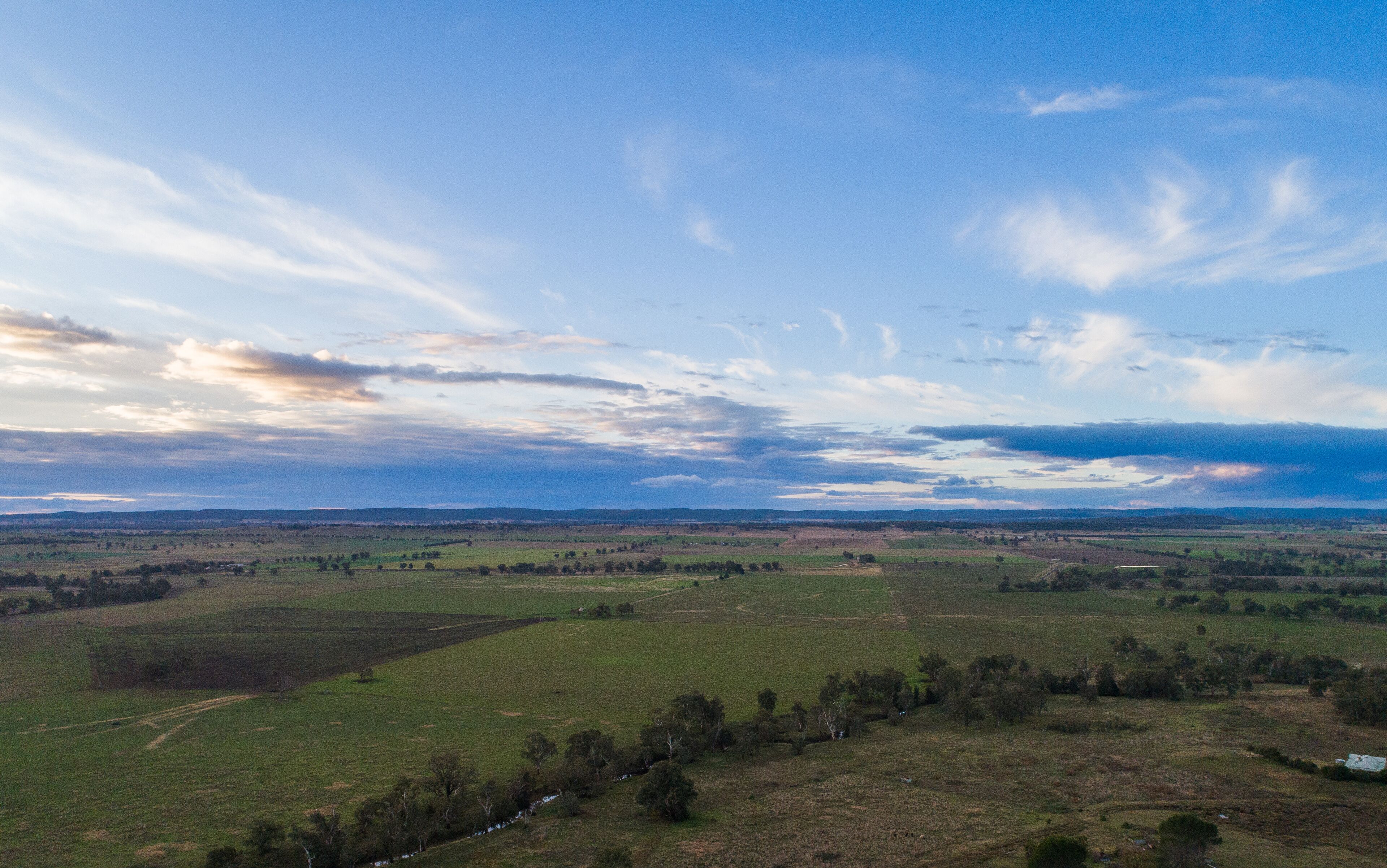 A vast landscape with rolling hills, a river, and a clear sky with scattered clouds.