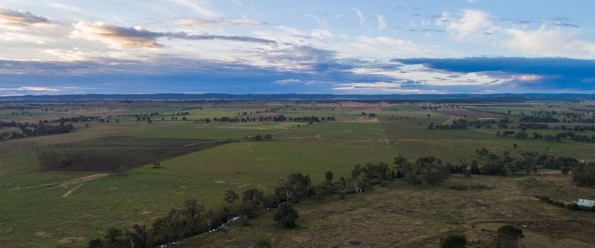 A vast landscape with rolling hills, a river, and a clear sky with scattered clouds.
