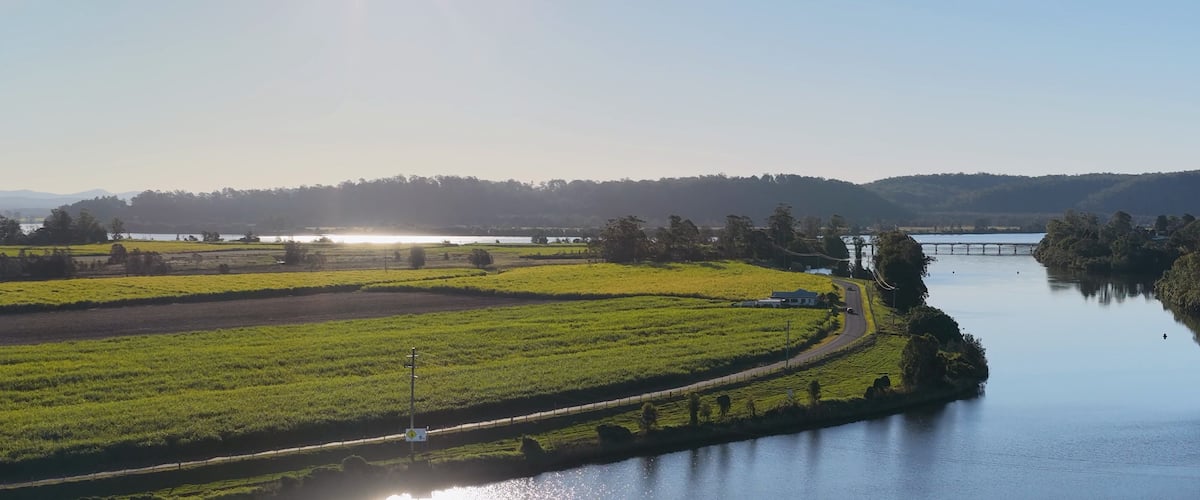 A river with a bridge, green fields, and a clear sky.