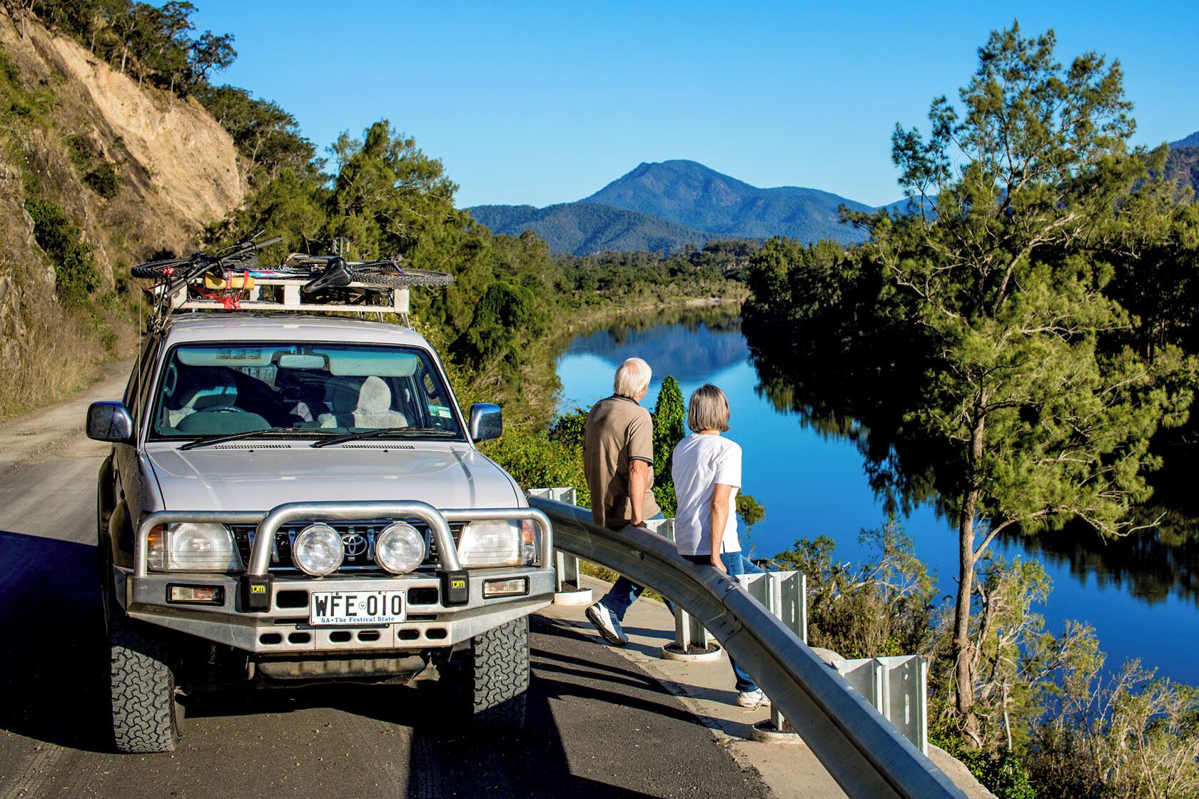 A silver SUV with a license plate WFE 010 parked by a lake with two people standing beside it.