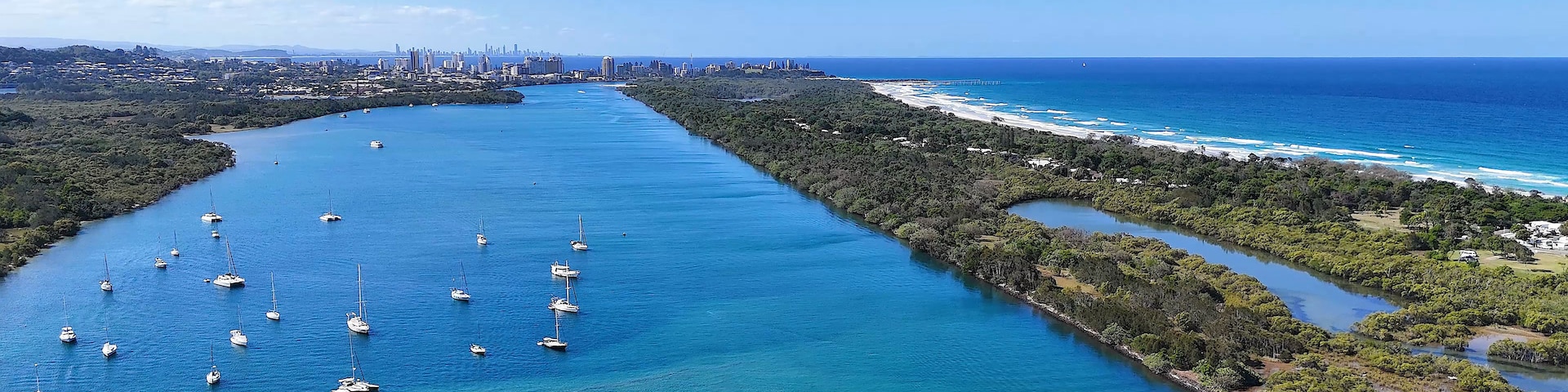 Eine Küstenstadt mit einem Yachthafen voller Segelboote, einem dichten Waldgebiet und einem klaren, blauen Ozean.