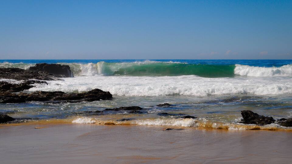 A beach with waves crashing against rocks and a clear blue sky.