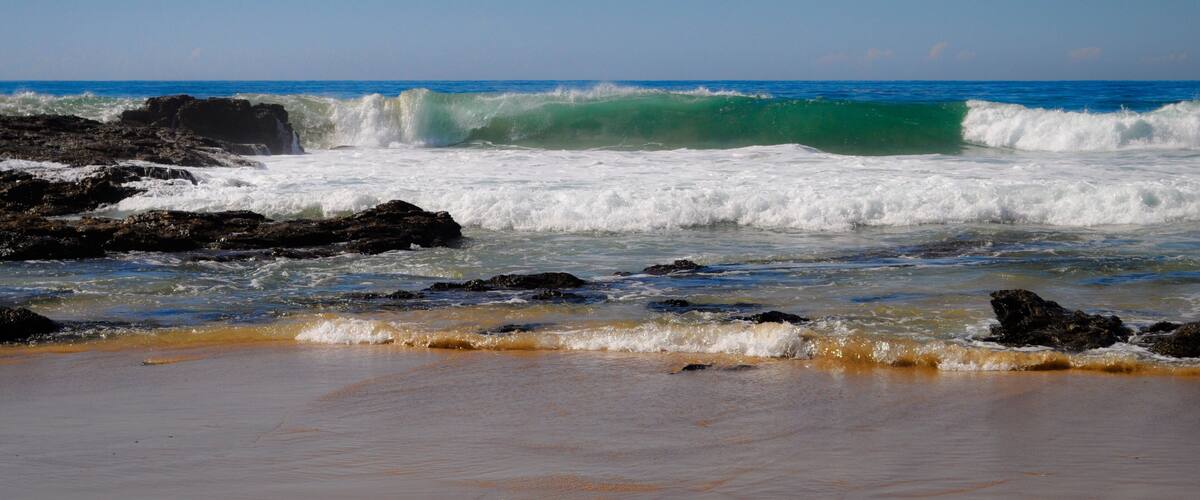 A beach with waves crashing against rocks and a clear blue sky.