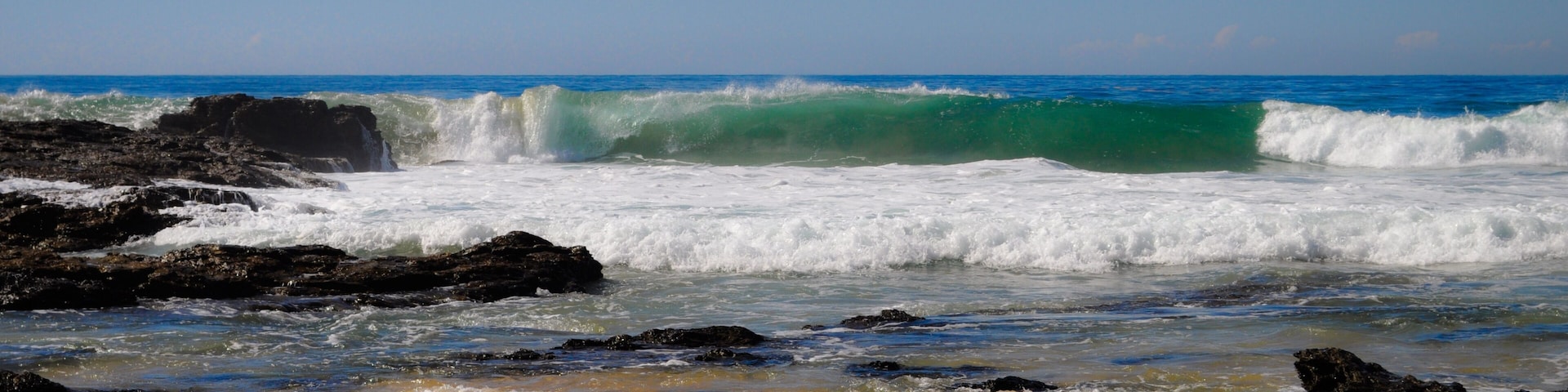 A beach with waves crashing against rocks and a clear blue sky.