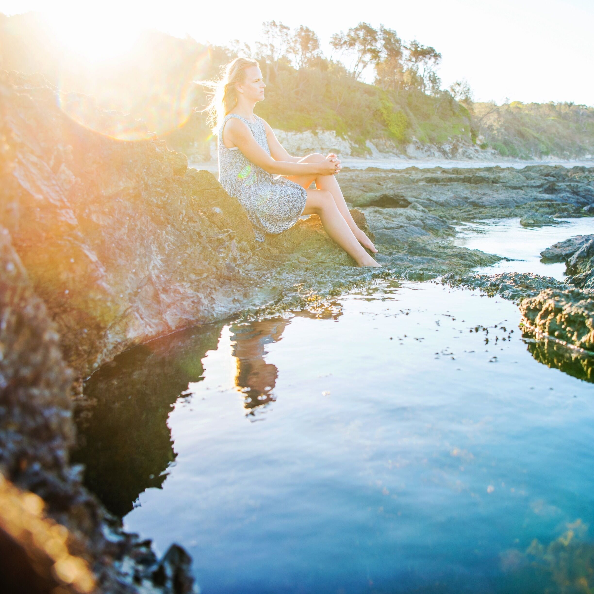 A person sitting on a rock by a calm body of water with trees in the background.