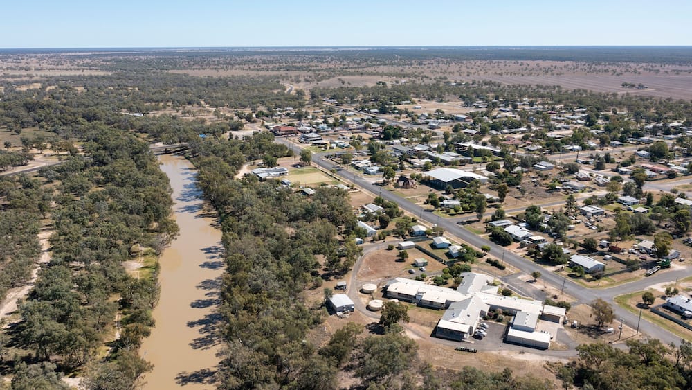 An aerial view of a town with a river, surrounded by dense forests and open fields.