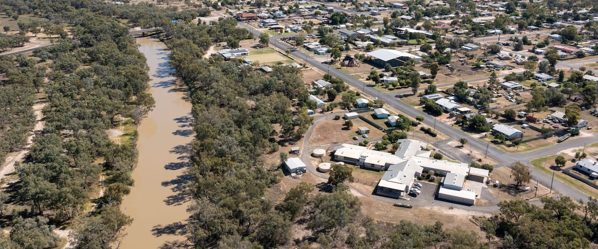 An aerial view of a town with a river, surrounded by dense forests and open fields.