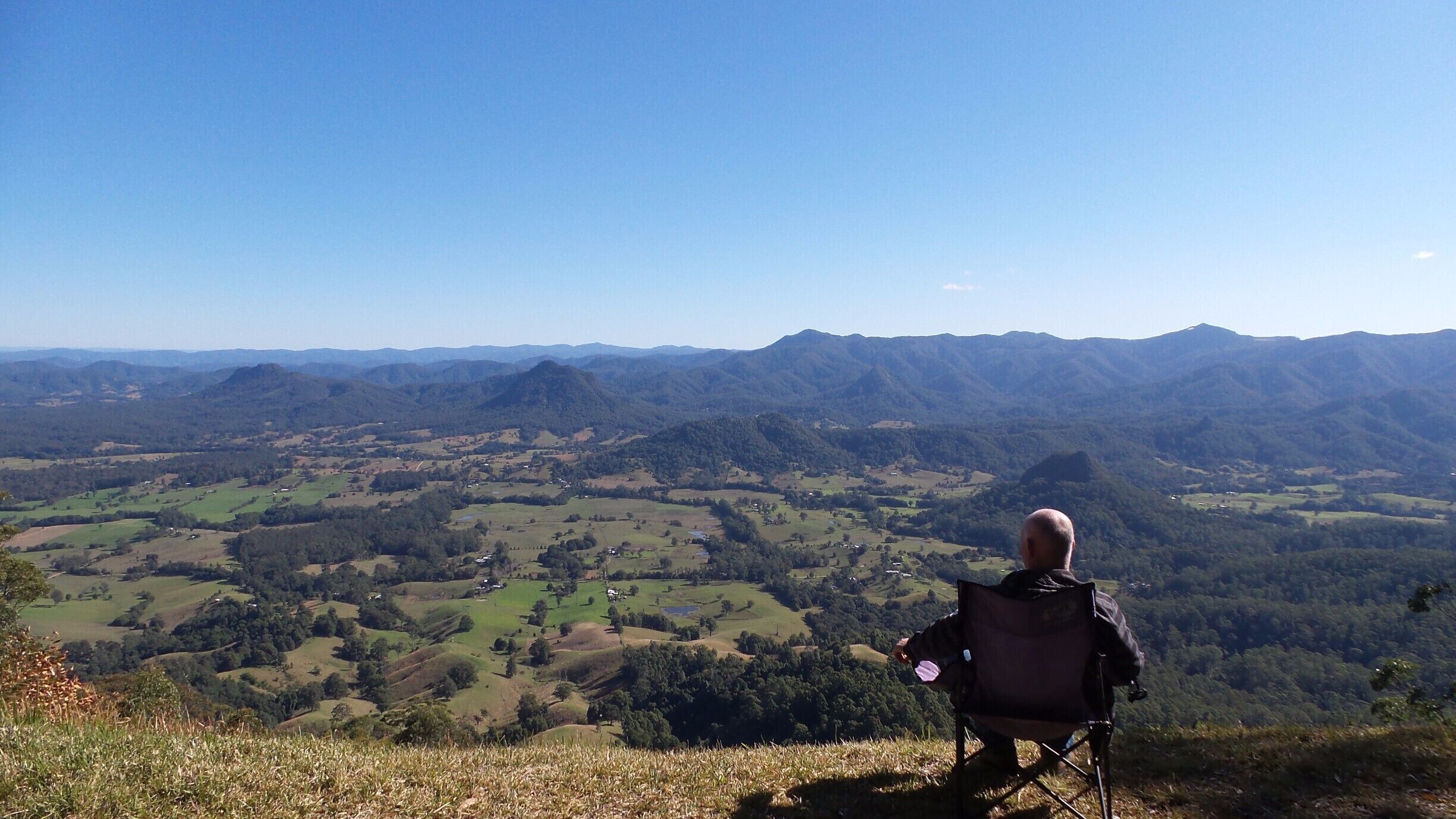 A person in a chair overlooking a valley with rolling hills and distant mountains.
