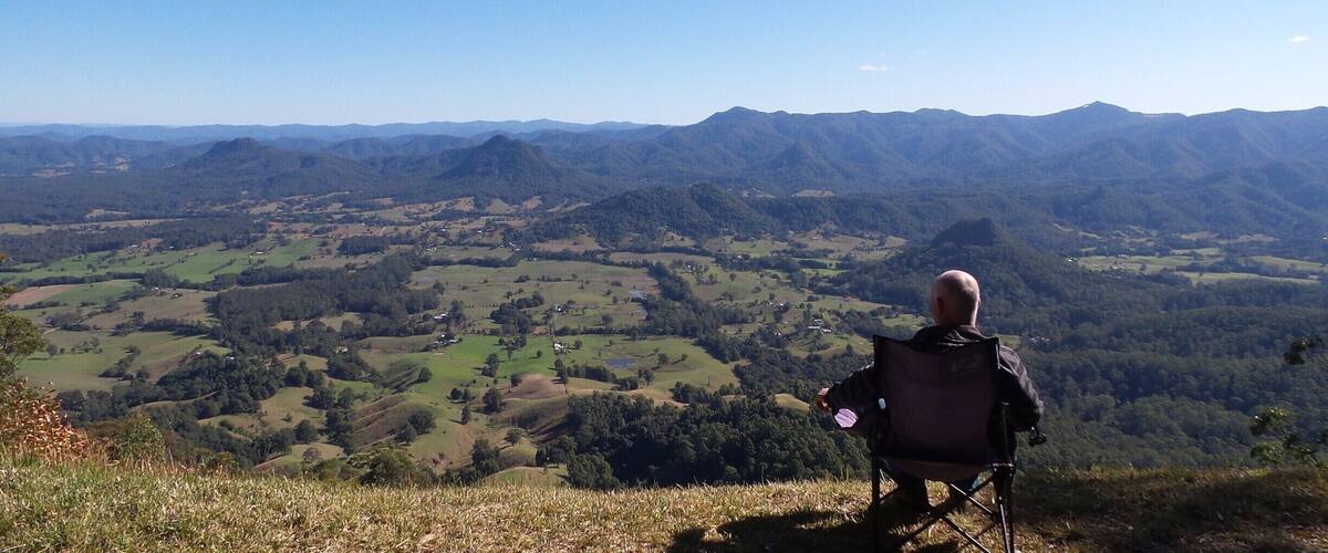 A person in a chair overlooking a valley with rolling hills and distant mountains.