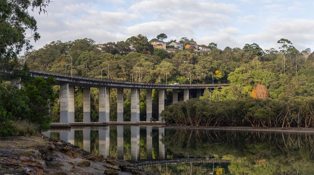 A bridge over a calm river with a forested hillside in the background.