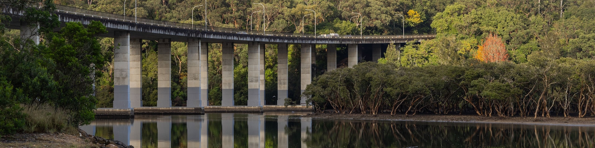 Un pont enjambant une rivière paisible, avec une colline boisée en arrière-plan.