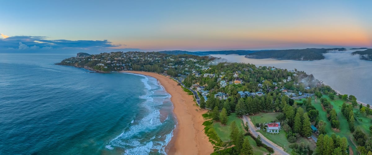 A coastal landscape with a beach, a golf course, and a forested area.