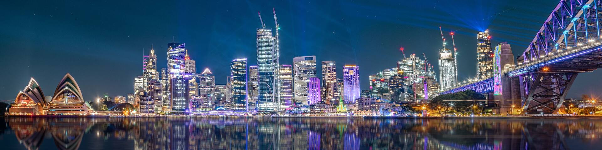 A city skyline at night with illuminated buildings and a bridge.