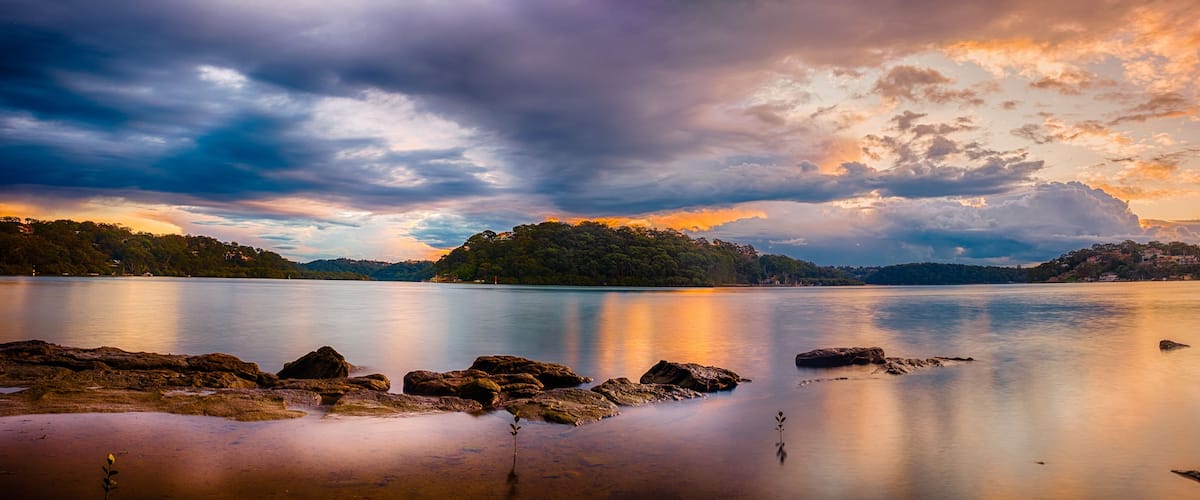 A calm lake with rocky shores, a forested island, and a sunset sky.