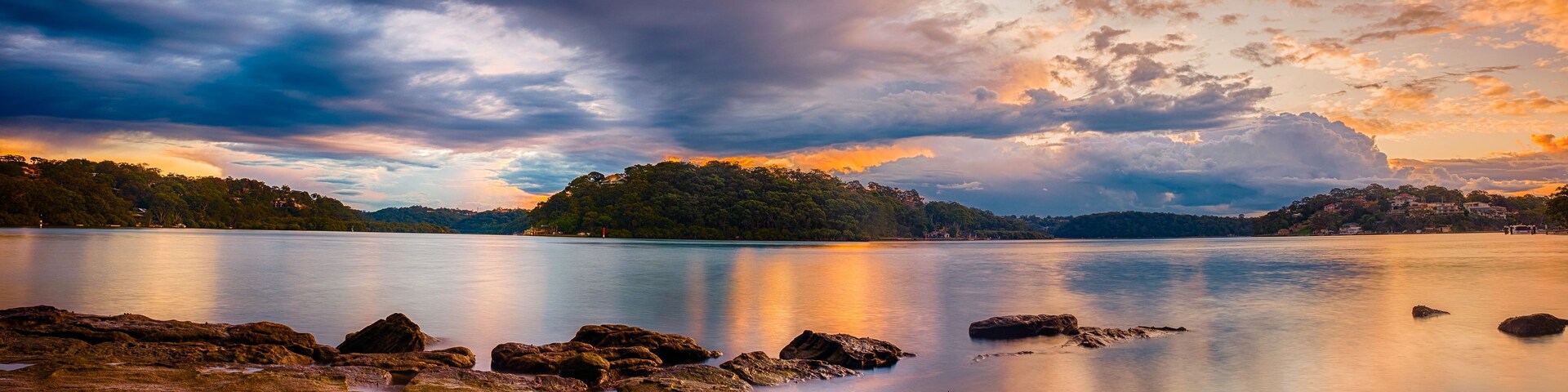 Un lago tranquilo con costas rocosas, una isla boscosa y un cielo al atardecer.