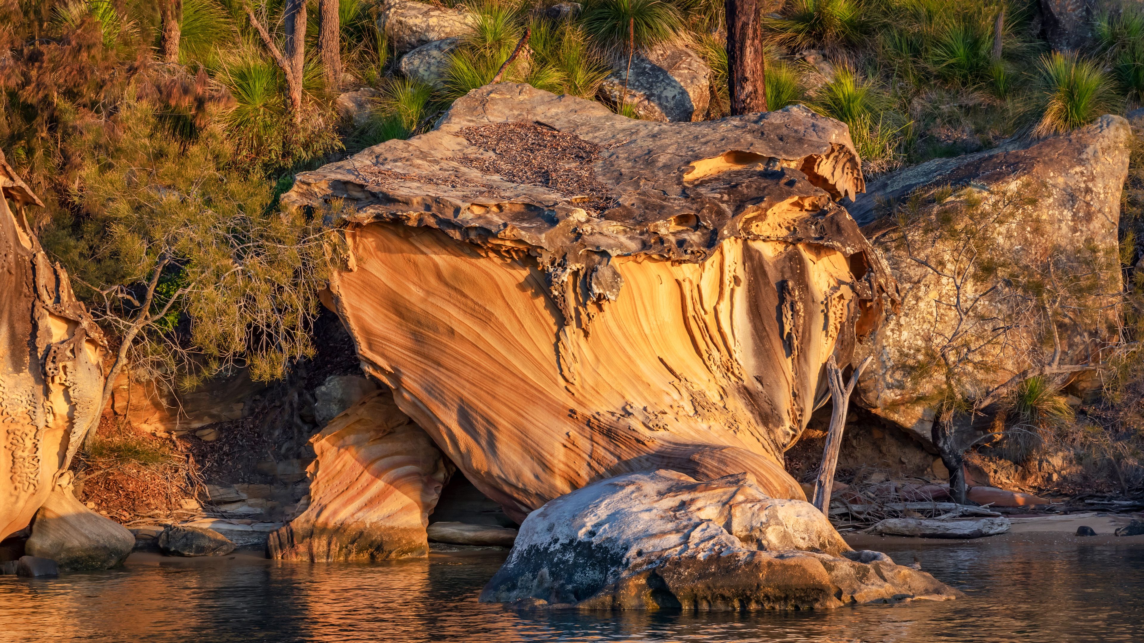 A large rock formation with a river flowing around it, surrounded by greenery and trees.